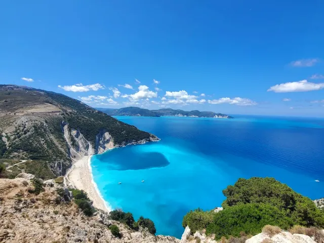 A high view over a bay of vivid turquoise water, with a white shore strip and green cliffs