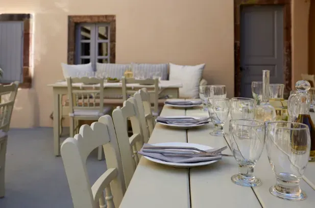 A long cream toned wooden table, set with glasses and napkins in a quiet courtyard