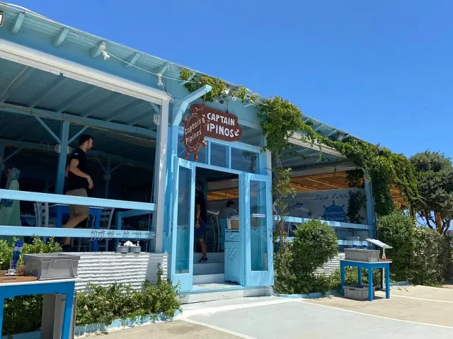 A blue and white building with a canopy, a climbing vine and a round sign above the entrance