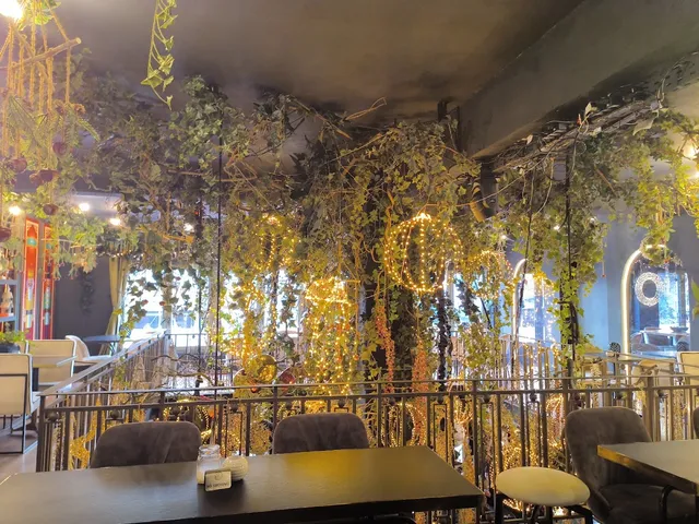 A seating hall with climbing greenery and golden string lights above a metal railing