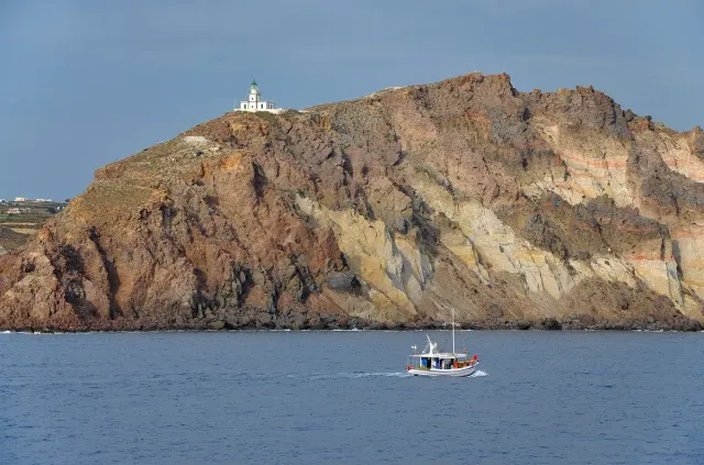 A high rocky cape with a white lighthouse at its tip and a boat passing in the sea below