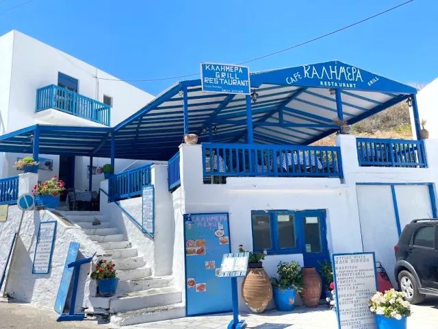 A blue and white building with a blue pergola, stairs, menu boards and flowering blue pots