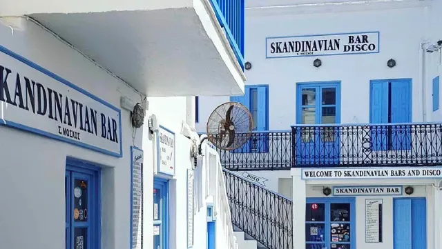 White houses with blue shutters, an iron staircase and bar signs on the facades