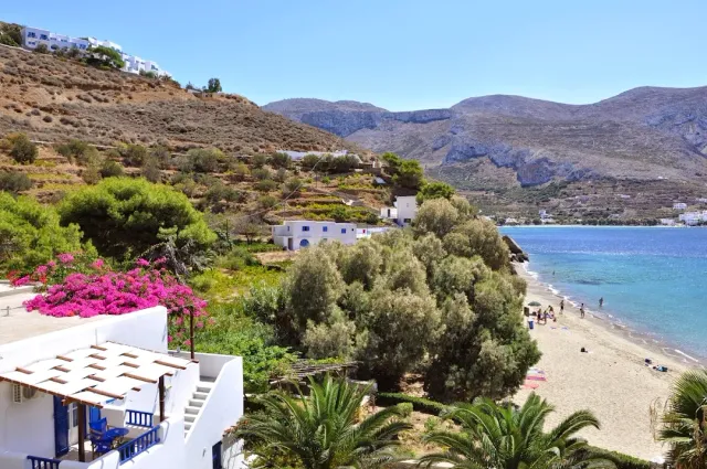 A white terrace with pink bougainvillea, and below it a sandy beach, sea and bare mountains
