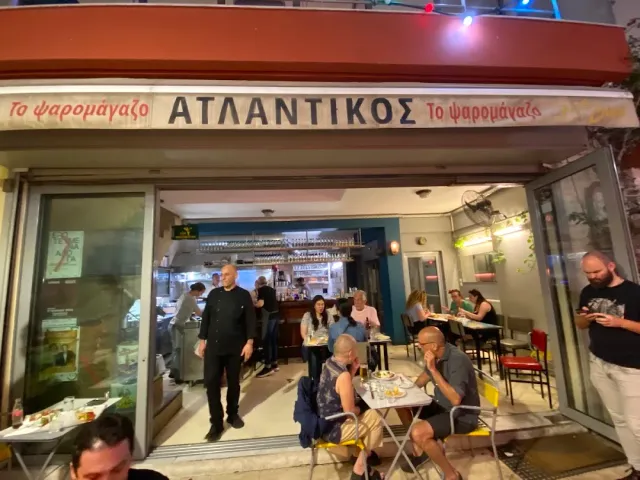 An open frontage at night with a red sign, small tables and diners on the pavement