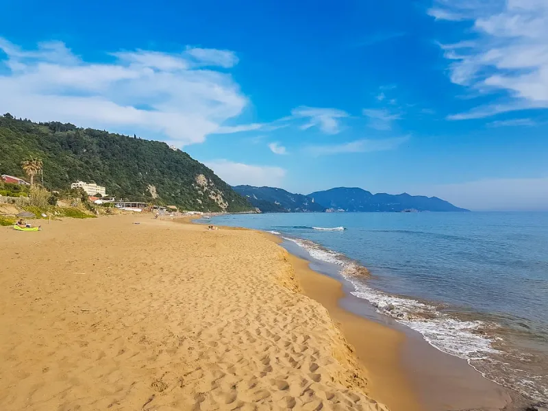 Glyfada beach on Corfu, golden sand and surf below a green headland