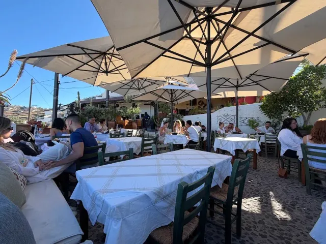 Tables in white cloths under large parasols, with green chairs and diners