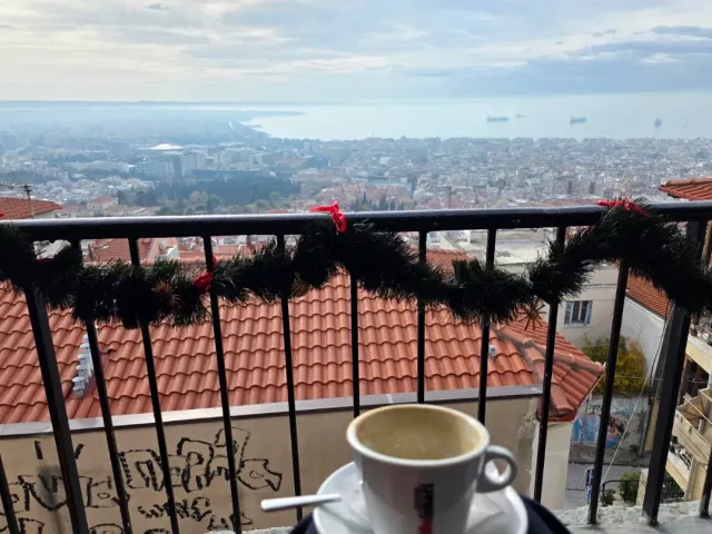 A coffee cup on a decorated balcony railing, with tiled roofs and the city down to the sea below