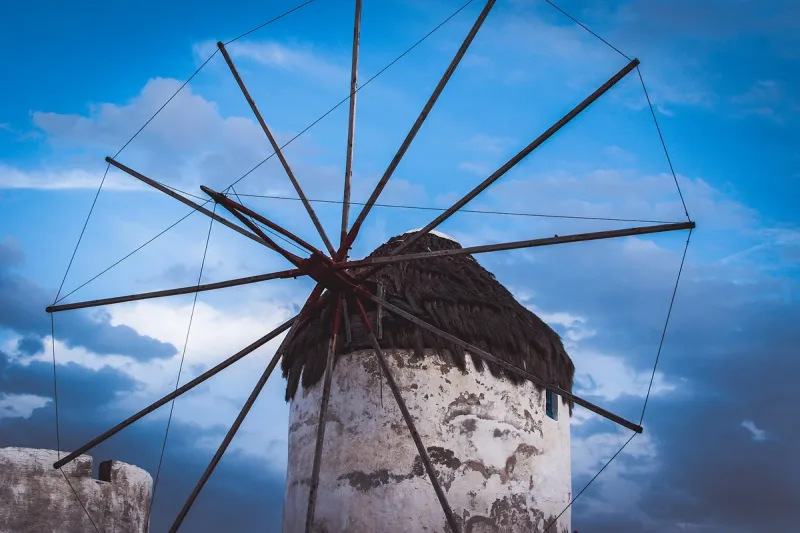 A whitewashed windmill with wooden sails against a blue sky