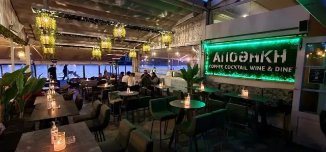 An interior in green lighting with hanging lamps, armchairs and round tables