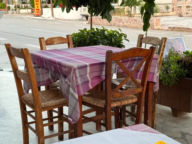 An outdoor table with a purple checked cloth, wooden chairs with straw seats and pots beside it