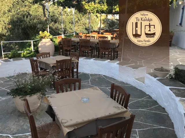 A stone courtyard with wooden tables, a large clay jar and a round sign on the wall