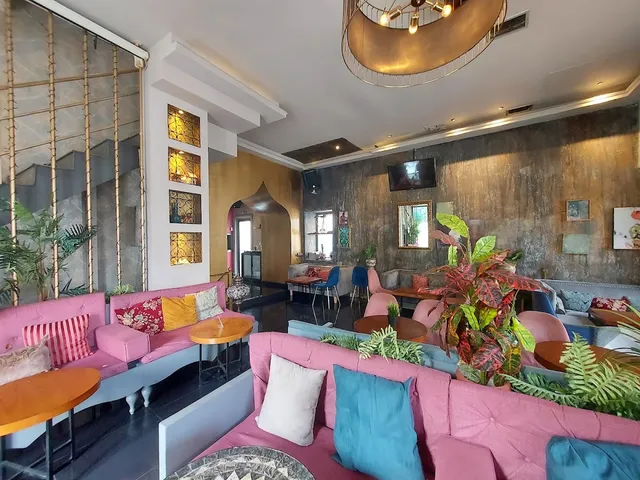 A lounge with pink sofas, colourful cushions, plants and an oriental style arch