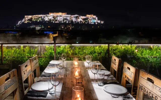 A wooden table set with candles on a roof, with a lit hill and a temple behind at night