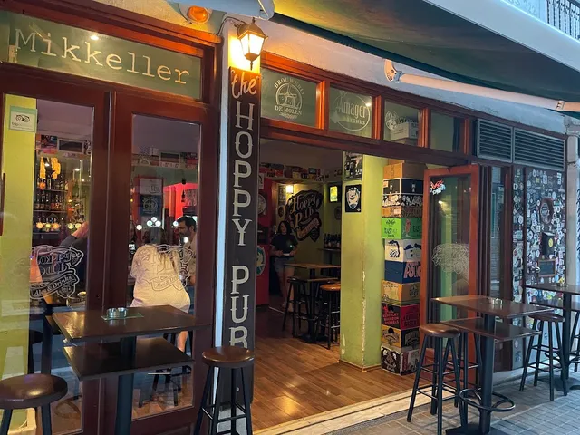 A pub entrance with a vertical sign post, high tables and walls covered in beer labels