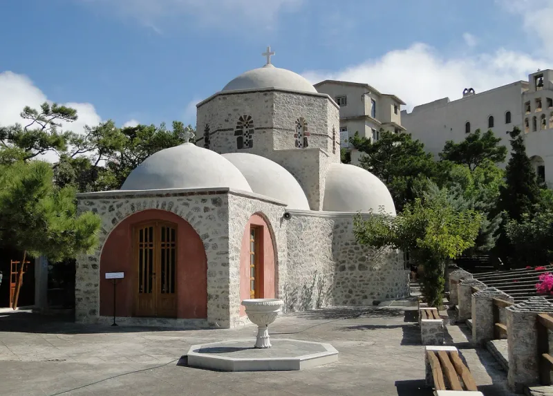 A stone church with white domes and a paved courtyard with a small fountain