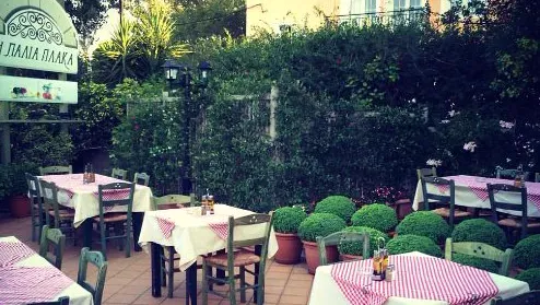 A green courtyard with red checked tablecloths, a hedge and potted plants