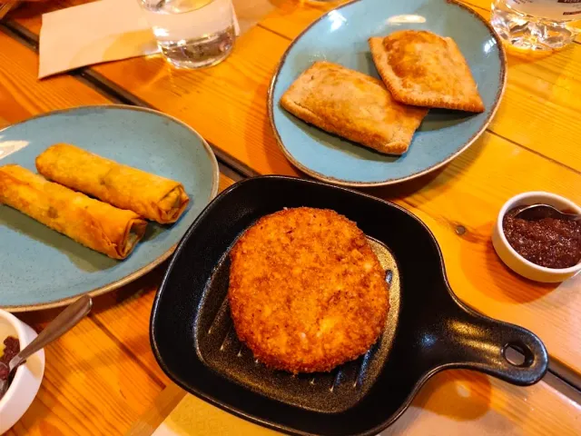 A cast iron pan with a fried patty, beside it crisp rolls and baked turnovers