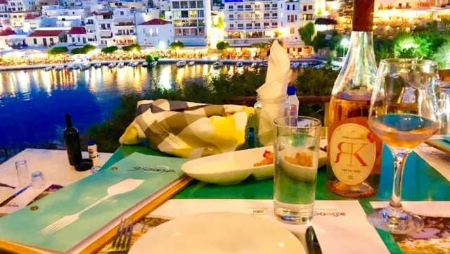 A set table with a bottle of wine, facing a lit bay in the evening