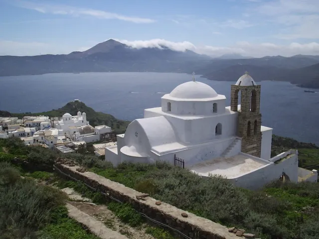 A white church with a blue dome on a hilltop, with a bay and hills behind it