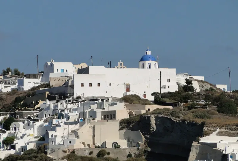 Whitewashed houses clinging to a cliff edge around a church with a blue dome
