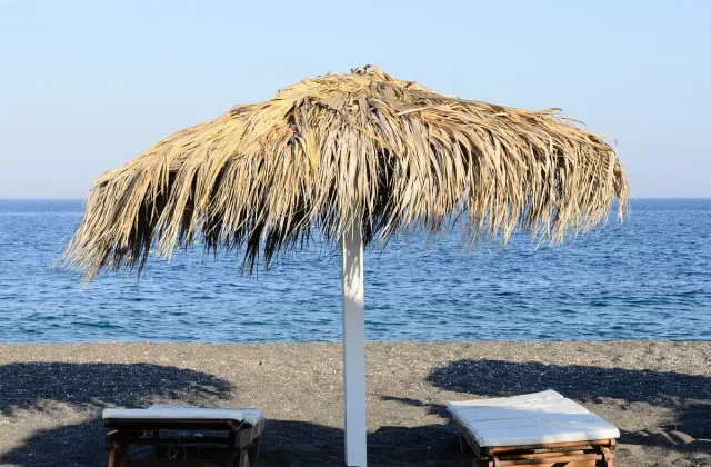 A straw parasol and two sunbeds on black sand facing blue sea