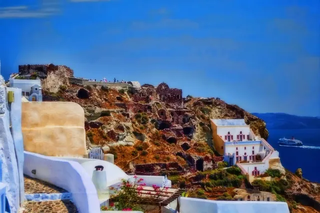 Fortress ruins on a rocky spur, white houses around them and deep blue sea below