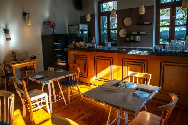 An interior lit warmly with a wooden counter, grey tables and mismatched chairs