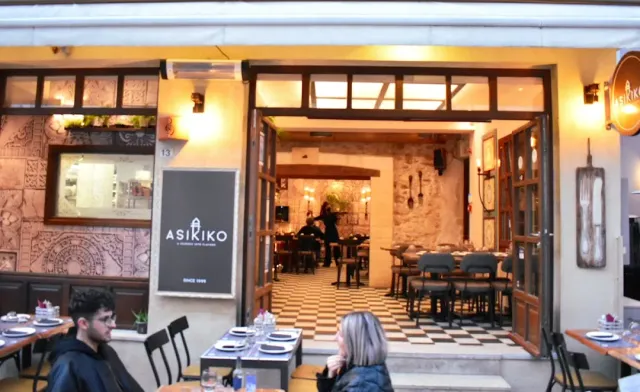 A lit frontage with an open door onto a chequered floor, and outdoor tables with people seated