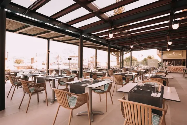 A covered terrace with a metal pergola, wicker chairs with turquoise cushions and laid tables