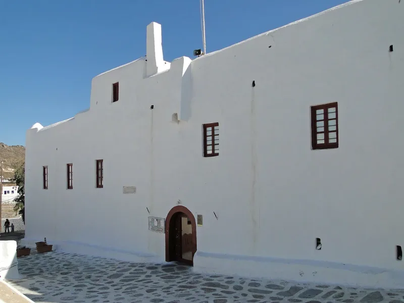 A whitewashed building with an arched wooden door and a cobbled square