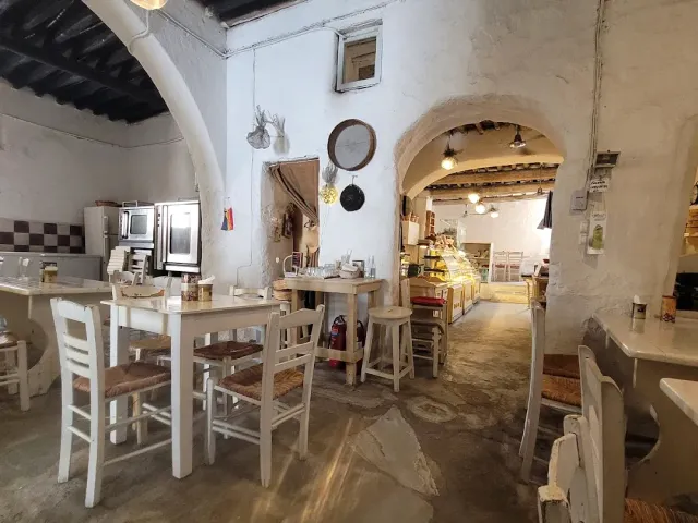 A whitewashed space with stone arches, white tables and stools and a display case beyond