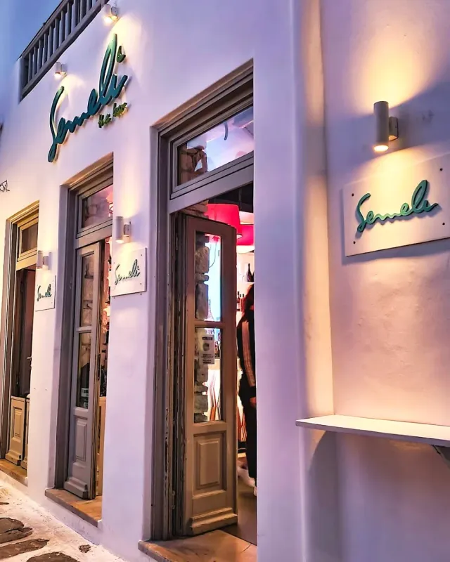 A whitewashed front in an alley with green script signs and lit doorways in the evening