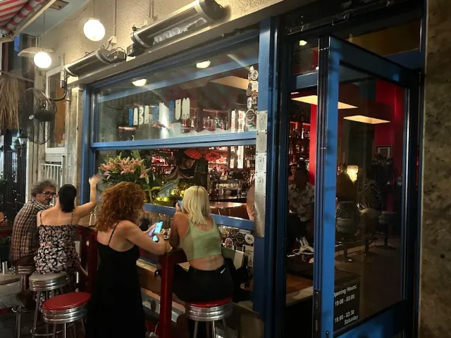 People on red stools at a bar window open to the street in the evening