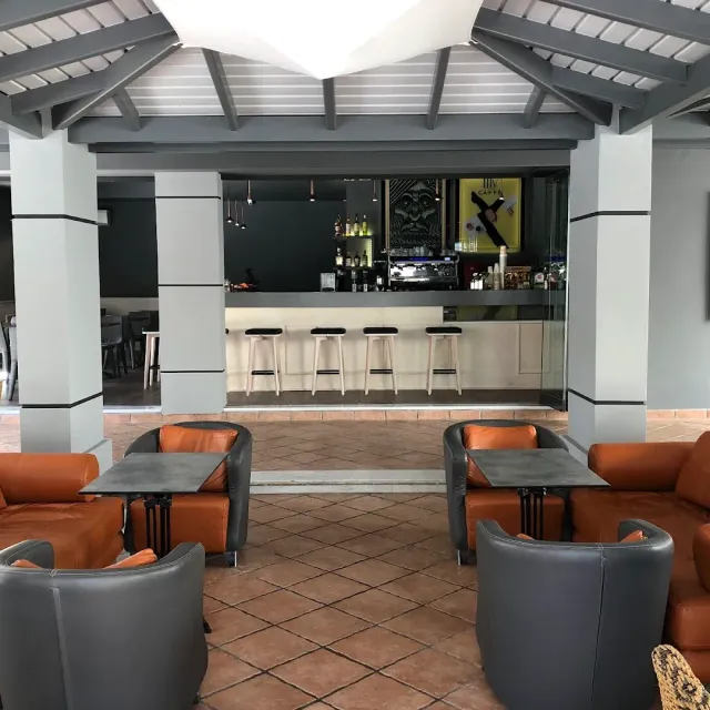 A covered lounge with orange and grey leather armchairs, low tables and a counter with stools