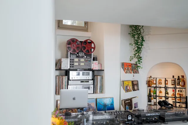 A DJ booth with a reel to reel recorder, record shelves and a bottle shelf in a white niche