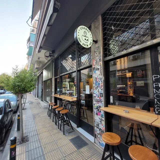 A street bar front with a round sign, wooden counters along the windows and stools on the pavement