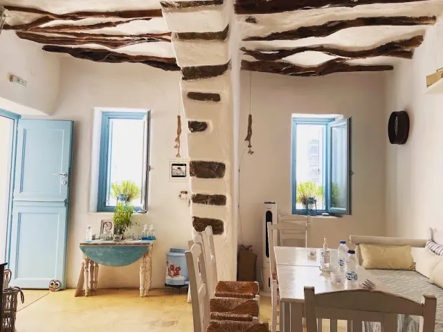 A whitewashed room with wooden ceiling beams, a light blue door and windows and white tables