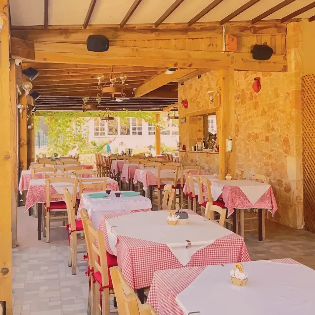 A terrace covered by heavy wooden beams, red checked tablecloths, wooden chairs and a stone wall