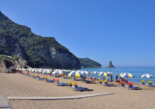 Rows of colourful parasols on a sandy beach between green cliffs and calm sea