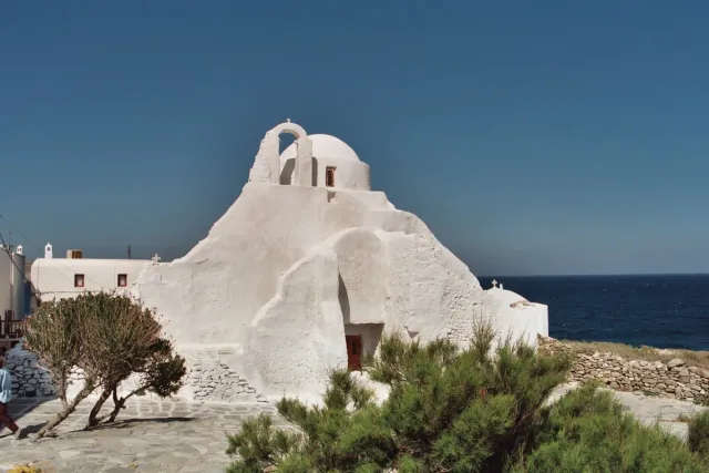 A whitewashed church of rounded asymmetric shapes against blue sea