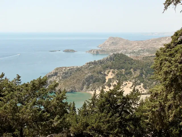 A high view over a bay with a long sandy beach, green hills and the sea