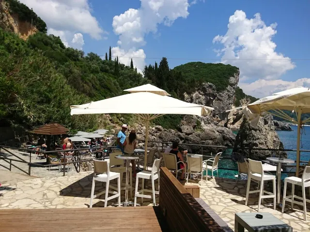 White parasols and bar chairs on rock steps, above turquoise water between cliffs