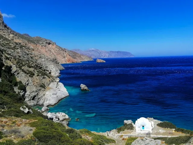 Steep cliffs dropping to a deep blue sea, with a small white chapel on the rocks