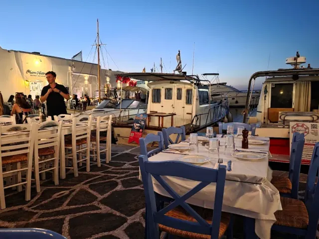 Tables set on a stone quay at dusk, with fishing boats moored behind