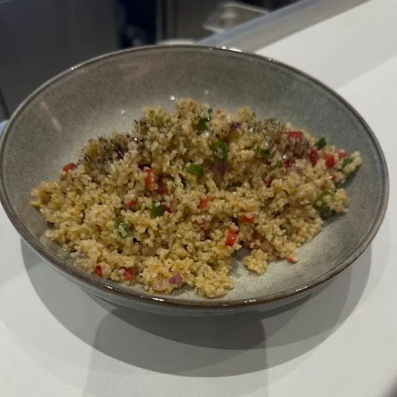 A grey bowl of bulgur salad with chopped vegetables on a white counter