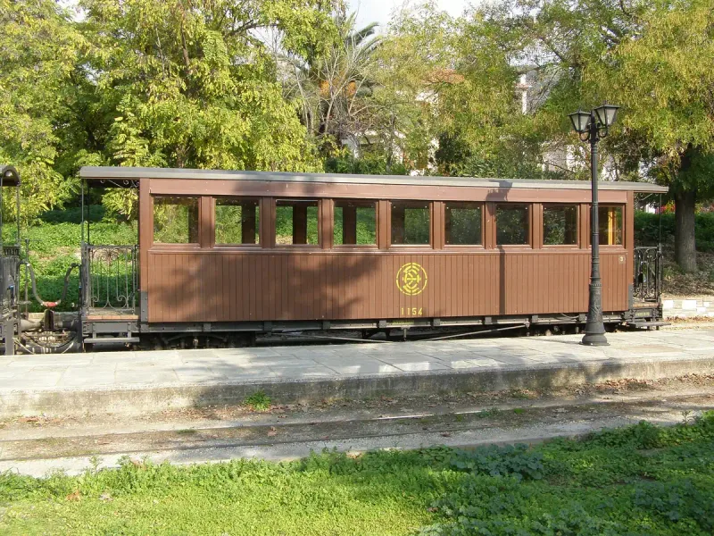 A brown wooden narrow gauge railway carriage standing by a platform among trees