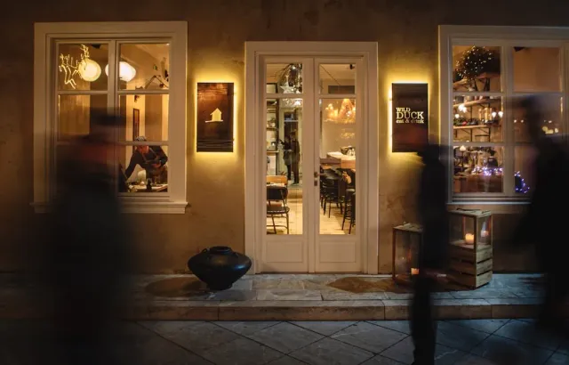 A frontage lit at night with a glass door, a floor lantern and blurred passersby