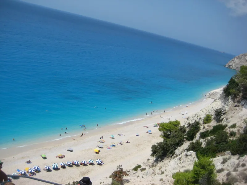 A view from above of a turquoise bay with a white cliff and umbrellas on the sand