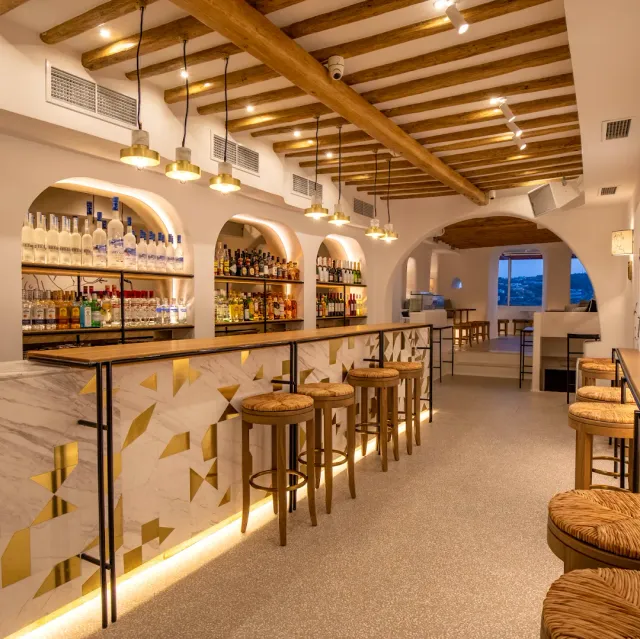 A marble counter with gold detailing, wicker stools and arched niches holding bottles